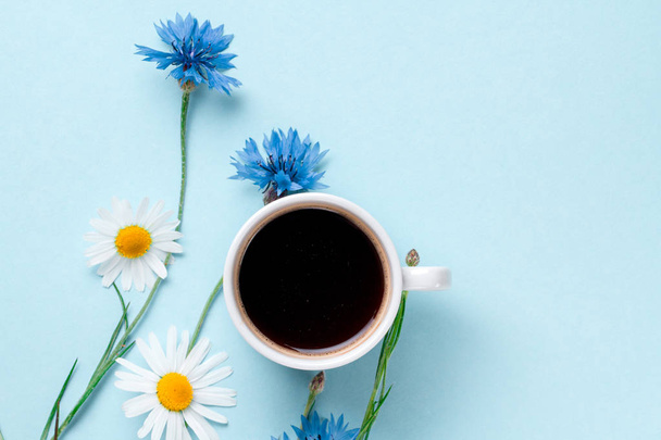 Spring background. Cornflowers, chamomile and a cup of hot coffee on a blue background. Top view  - Foto, imagen