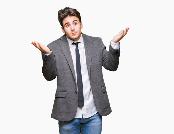 Young business man wearing suit and tie over isolated background clueless and confused expression with arms and hands raised. Doubt concept. - Photo, Image