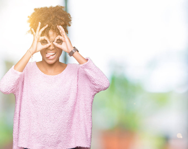 Hermosa mujer afroamericana joven con gafas sobre un fondo aislado haciendo buen gesto como prismáticos sacando la lengua, ojos mirando a través de los dedos. Expresión loca
. - Foto, Imagen