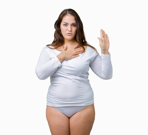 Beautiful plus size young overwight woman wearing white underwear over isolated background Swearing with hand on chest and open palm, making a loyalty promise oath - Photo, Image
