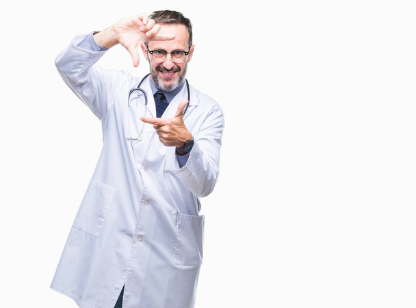 Старший седовласый врач средних лет в медицинской форме на изолированном фоне улыбается делая рамку с руками и пальцами с счастливым лицом. Концепция творчества и фотографии
. - Фото, изображение