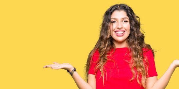 Mooie jongedame dragen casual t-shirt Smiling tonen dat beide handen open palmen, presentatie en reclame vergelijking en evenwicht - Foto, afbeelding