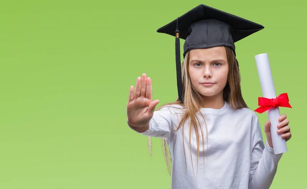 Młoda piękna dziewczyna czapce absolwent posiadający stopień na białym tle z otwarcia strony wykonują znak stop z poważnych i pewnie wyrażenie, obrony gest - Zdjęcie, obraz