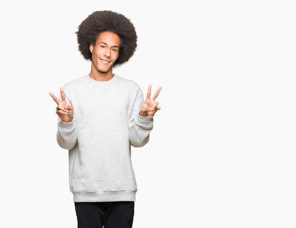 Giovane uomo afro americano con i capelli afro indossare felpa sportiva sorridente guardando la fotocamera mostrando le dita facendo segno di vittoria. Numero due.
. - Foto, immagini