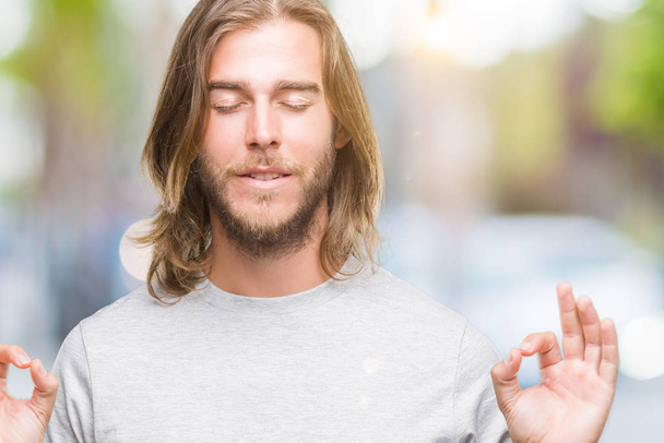 分離の背景の上の長い髪の若いハンサムな男リラックスして瞑想の指ジェスチャーをやって閉じた目と笑顔します。ヨガの概念. - 写真・画像