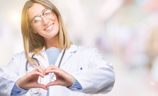 Young beautiful doctor woman headphones over isolated background smiling in love showing heart symbol and shape with hands. Romantic concept. - Фото, изображение