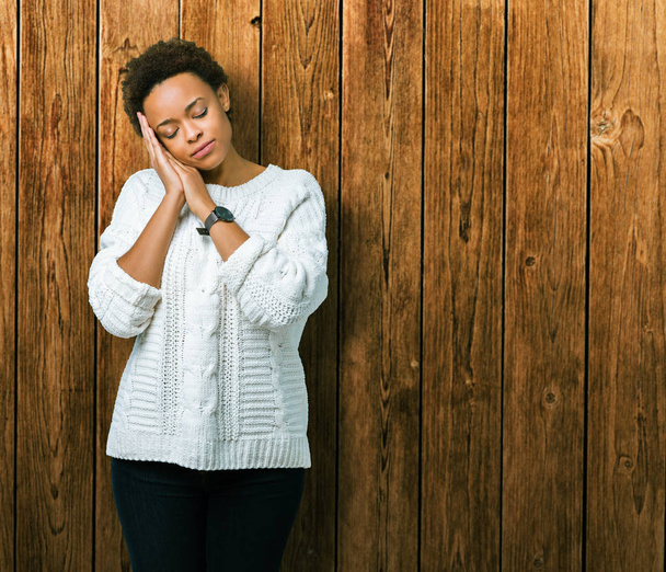 Piękne młode african american kobieta sobie sweter na białym tle spania zmęczony marzy i pozowanie ręce razem jednocześnie uśmiechając się z zamkniętymi oczami. - Zdjęcie, obraz