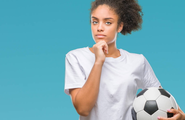 Молодой красивый афро-американец держит футбольный мяч на изолированном фоне серьезное лицо, думая о вопросе, очень запутанная идея
 - Фото, изображение