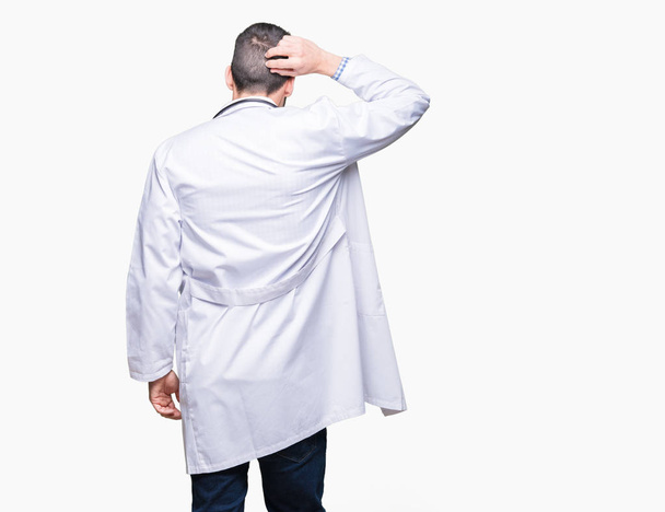 Knappe jonge dokter man over geïsoleerde achtergrond terug denken over twijfel met hand op hoofd - Foto, afbeelding
