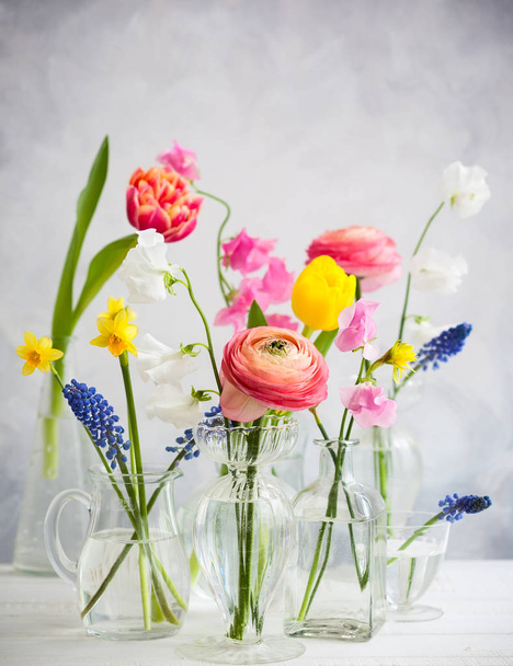 Beautiful flowers bouquets in glass vases on the wooden table.Tulips,roses,muscari, narcissus, eustoma and hyacinths - Fotoğraf, Görsel