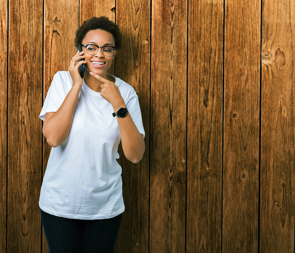 Joven mujer afroamericana hablando por teléfono sobre fondo aislado muy feliz señalando con la mano y el dedo
 - Foto, Imagen