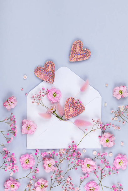 Spring floral composition made of fresh pink flowers,envelope and hearts on light pastel background. Festive flower concept. Flat lay, top view with copy space. - Фото, изображение
