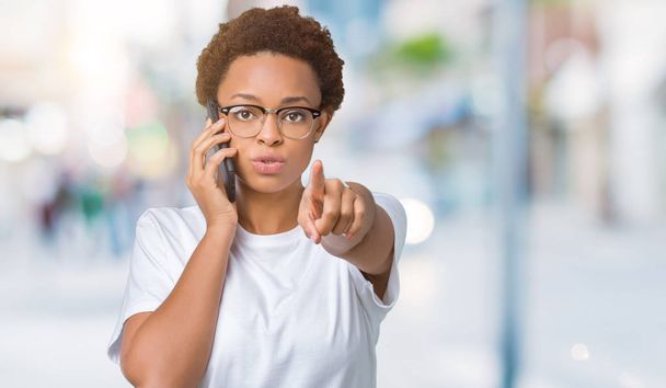 Jeune femme afro-américaine parlant au téléphone sur fond isolé pointant du doigt la caméra et vers vous, signe de la main, geste positif et confiant de l'avant
 - Photo, image