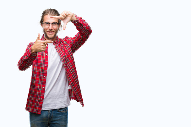 Young handsome man with long hair wearing glasses over isolated background smiling making frame with hands and fingers with happy face. Creativity and photography concept. - Photo, Image