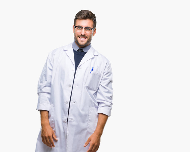 Молодой привлекательный мужчина, носящий доктора, ученый в пальто на изолированном фоне смотрит в сторону с улыбкой на лице, естественным выражением лица. Смеясь уверенно
. - Фото, изображение