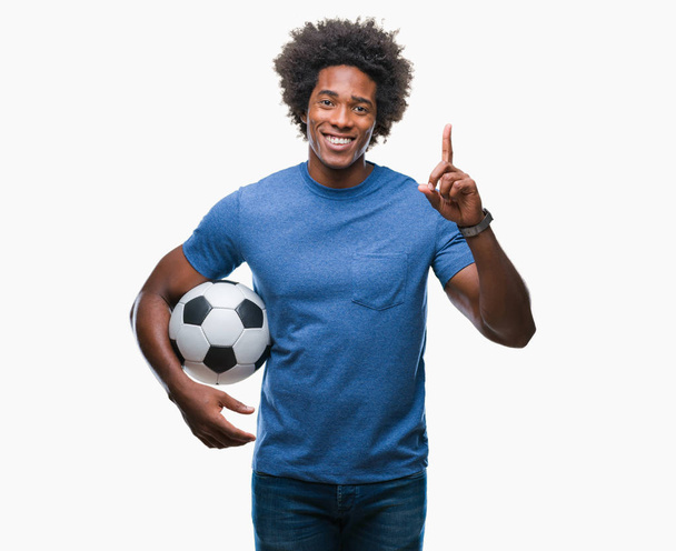 Afro americký muž hospodářství fotbal míč izolované pozadí překvapilo s nápad nebo otázku ukazující prst s šťastné tváře, číslo jedna - Fotografie, Obrázek
