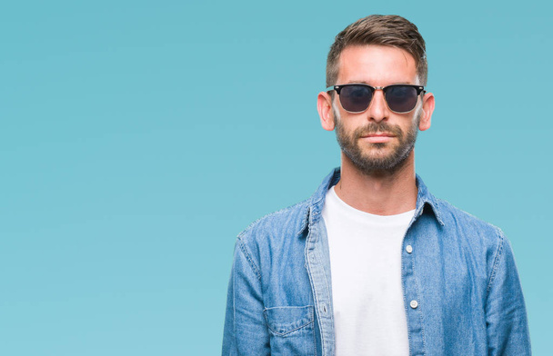 Young handsome man wearing sunglasses over isolated background with serious expression on face. Simple and natural looking at the camera. - Foto, afbeelding