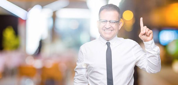 Middle age bussines arab man wearing glasses over isolated background showing and pointing up with finger number one while smiling confident and happy. - Foto, afbeelding