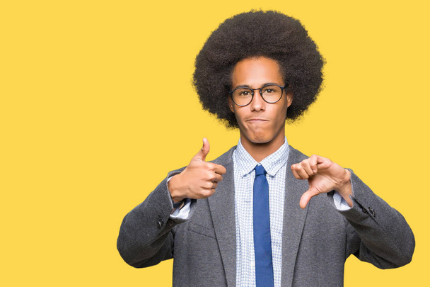 Jeune homme d'affaires afro-américain aux cheveux afro portant des lunettes Faire les pouces de haut en bas, désaccord et expression d'accord. Conflit fou
 - Photo, image