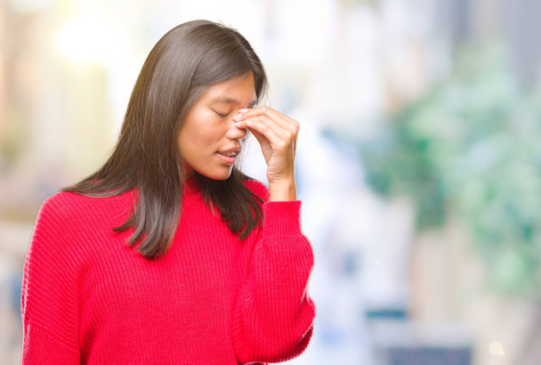 Молода азіатка в зимовому светрі над ізольованим тлом втомилася терти ніс і очі відчувають втому і головний біль. Концепція стресу та розчарування
. - Фото, зображення