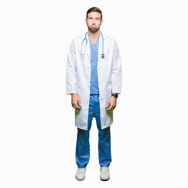 Knappe dokter man medische uniform dragen over geïsoleerde achtergrond puffend wangen met grappige gezicht. Mond opgeblazen met lucht, gek expressie. - Foto, afbeelding