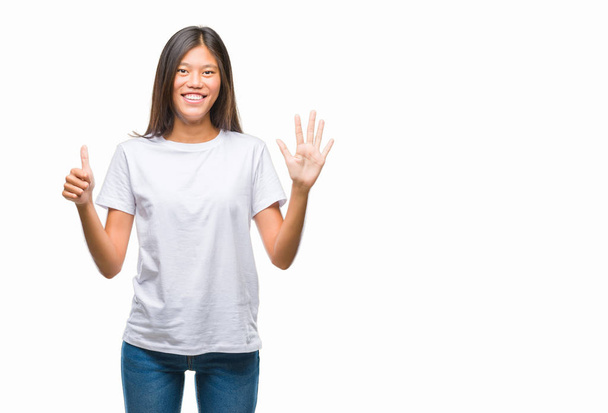 Jovem mulher asiática sobre fundo isolado mostrando e apontando para cima com os dedos número seis enquanto sorrindo confiante e feliz
. - Foto, Imagem