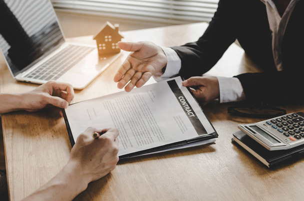 hand of young man customer signing contract for buying house with real estate broker in suit at estate agent office, investment, home loan contract, buying house, real estate and insurance concept - Photo, Image