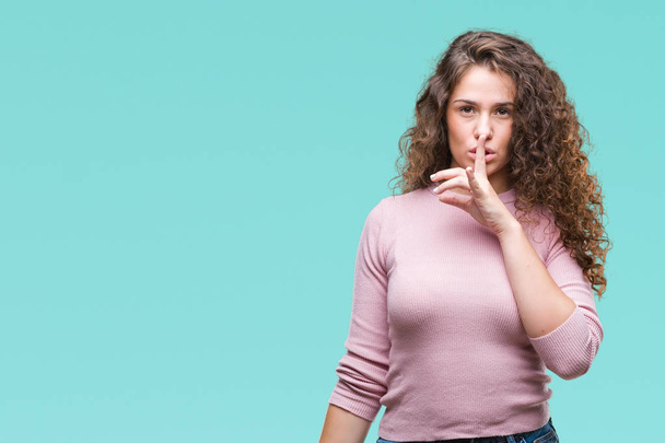 Beautiful brunette curly hair young girl wearing pink sweater over isolated background asking to be quiet with finger on lips. Silence and secret concept. - Foto, Imagen