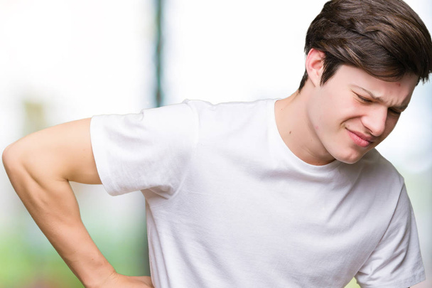 junger gutaussehender Mann in lässigem weißem T-Shirt über isoliertem Hintergrund, der unter Rückenschmerzen leidet, Rücken mit der Hand berührt, muskuläre Schmerzen - Foto, Bild