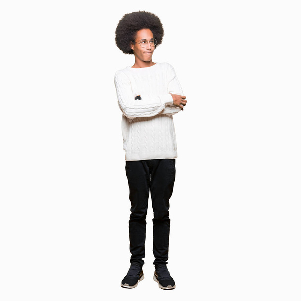 Young african american man with afro hair wearing glasses smiling looking to the side with arms crossed convinced and confident - Фото, изображение