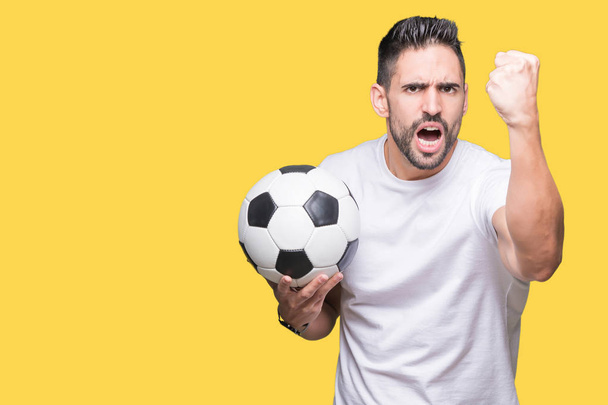 Young man holding soccer football ball over isolated background annoyed and frustrated shouting with anger, crazy and yelling with raised hand, anger concept - Foto, afbeelding