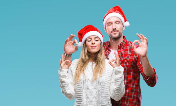 恋分離背景にクリスマス帽子をかぶっている若いカップルのリラックスし、瞑想の指ジェスチャーをやって閉じた目を浮かべてします。ヨガの概念. - 写真・画像