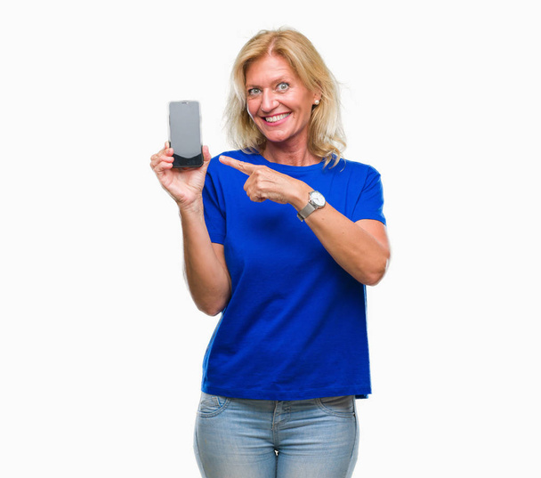 Middle age blonde woman showing blank screen of smartphone over isolated background very happy pointing with hand and finger - Photo, Image