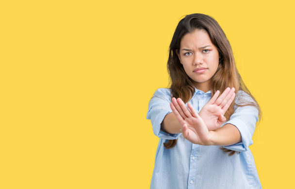 Young beautiful brunette business woman over isolated background Rejection expression crossing arms and palms doing negative sign, angry face - Photo, image