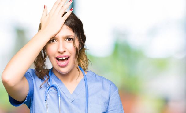 Giovane donna medico adulto indossando uniforme medica sorpreso con mano sulla testa per errore, ricordare l'errore. Dimenticato, concetto di cattiva memoria
. - Foto, immagini