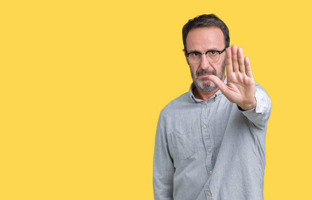 Handsome middle age elegant senior man wearing glasses over isolated background doing stop sing with palm of the hand. Warning expression with negative and serious gesture on the face. - Photo, Image