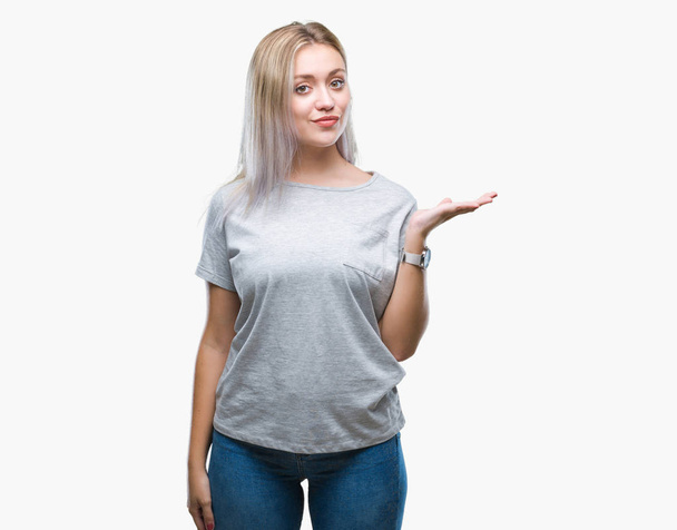 Young blonde woman over isolated background smiling cheerful presenting and pointing with palm of hand looking at the camera. - Fotografie, Obrázek