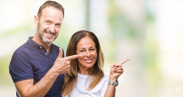 Middelbare leeftijd hispanic casual paar over geïsoleerde achtergrond glimlachen en kijken naar de camera met twee handen en vingers wijzen naar de kant. - Foto, afbeelding