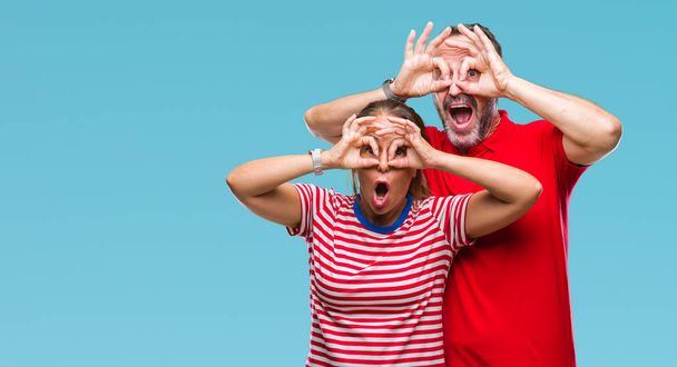 Středním věku hispánský pár v lásce izolované pozadí dělá ok gesto jako dalekohled držet jazyk, oči dívá skrze prsty. Šílený výraz. - Fotografie, Obrázek