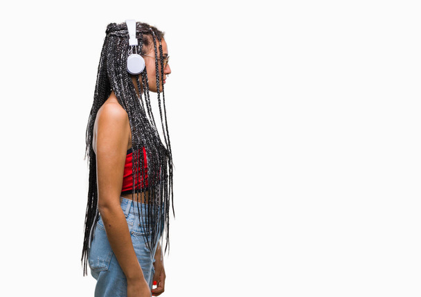 Молоде плетене волосся афроамериканка з позначкою народження в навушниках над ізольованим тлом, дивлячись в бік, розслабляє профільну позу з природним обличчям з впевненою посмішкою
. - Фото, зображення