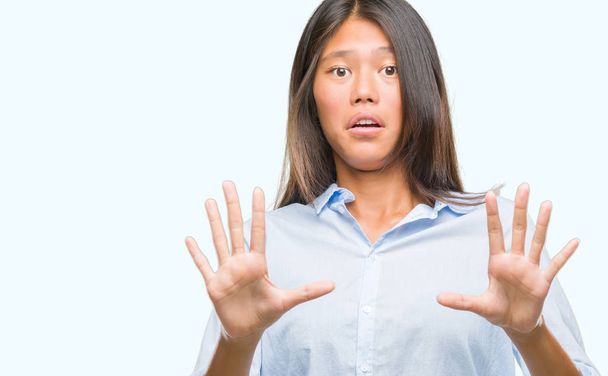 Young asian business woman over isolated background afraid and terrified with fear expression stop gesture with hands, shouting in shock. Panic concept. - Foto, Bild