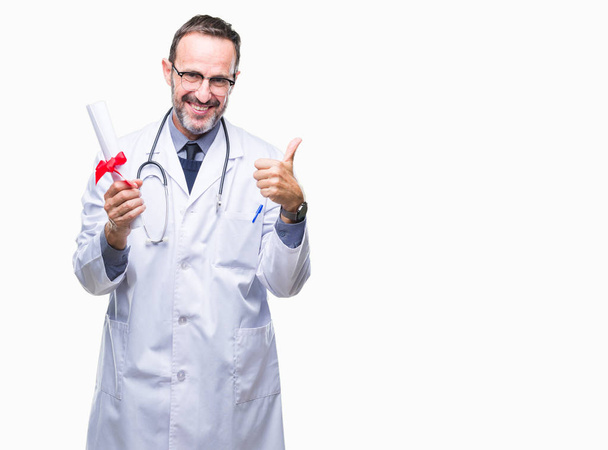 Orta yaş üst düzey ağarmış Doktor adam derecesi sertifika holding ok işareti, başparmak ile parmak, mükemmel işareti yapıyor kocaman bir gülümseme ile arka plan mutlu izole - Fotoğraf, Görsel