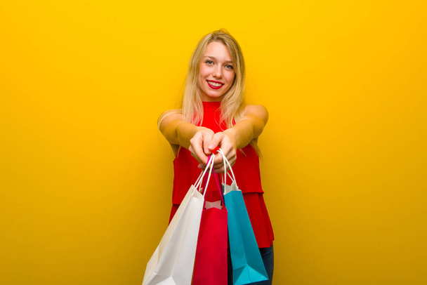 Jovem com vestido vermelho sobre a parede amarela segurando um monte de sacos de compras
 - Foto, Imagem