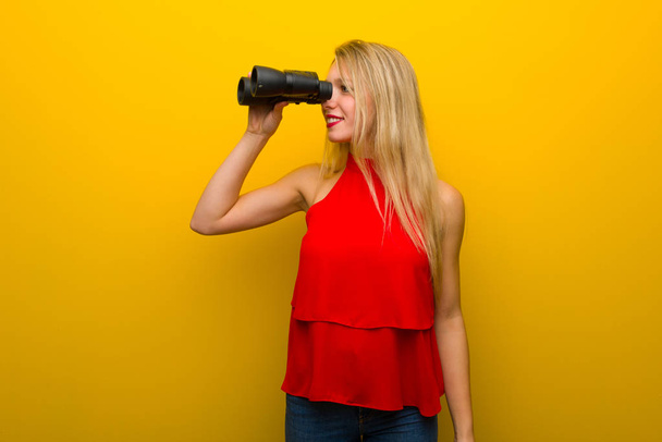 Giovane ragazza con vestito rosso sopra il muro giallo e guardando in lontananza con il binocolo
 - Foto, immagini