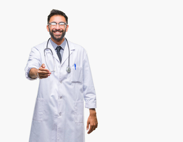 Ενηλίκων Ισπανόφωνος γιατρός άνθρωπος πέρα από το απομονωμένο υπόβαθρο χαμογελώντας προσφέροντας φιλική χειραψία ως χαιρετισμό και καλωσόρισμα. Επιτυχημένη επιχείρηση. - Φωτογραφία, εικόνα