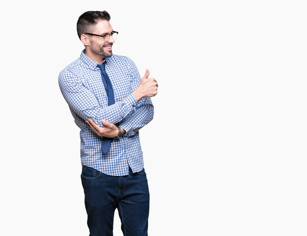 Молодой бизнесмен в очках на изолированном фоне выглядит гордым, улыбаясь делая большой палец вверх жестом в сторону
 - Фото, изображение