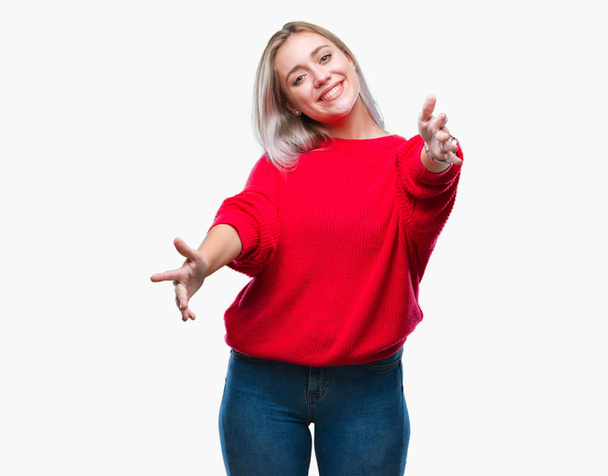 Young blonde woman wearing winter sweater over isolated background looking at the camera smiling with open arms for hug. Cheerful expression embracing happiness. - Photo, image