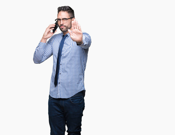 Молодий бізнесмен розмовляє по телефону над ізольованим фоном з відкритою рукою робить знак зупинки з серйозним і впевненим виразом, жест захисту
 - Фото, зображення