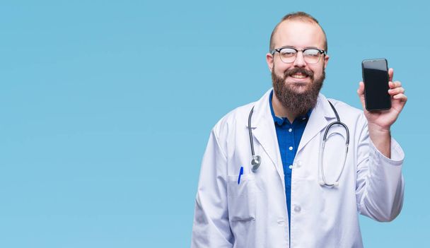 Jovem médico homem mostrando tela do smartphone sobre fundo isolado com um rosto feliz de pé e sorrindo com um sorriso confiante mostrando dentes
 - Foto, Imagem