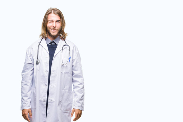 Young handsome doctor man with long hair over isolated background winking looking at the camera with sexy expression, cheerful and happy face. - Fotografie, Obrázek